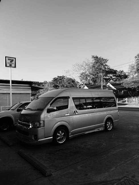 A mustard yellow vintage van parked on the pavement outside a residential property with white exterior walls and large windows. Behind the van, there is a large tree with yellow and green leaves, indicating autumn. The van appears to be used for home relocation or furniture transport, fitting within the context of removal services. The scene is well-lit with natural daylight, and the area looks calm and orderly. This image illustrates a typical setting for a house removals or moving company, such as Man with Van South Norwood, preparing for a local move along Station Road SE25, where careful loading and packing of belongings may take place inside or outside the property prior to transportation.